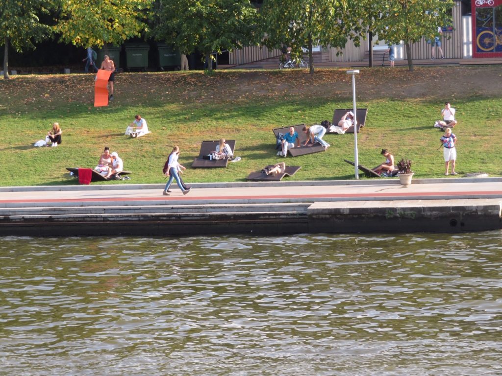 people walking while people sit in a field next to a pond